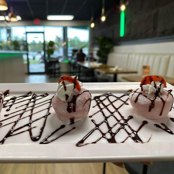 Two strawberry mochi desserts with whipped cream, chocolate drizzle, and a restaurant interior in the background.