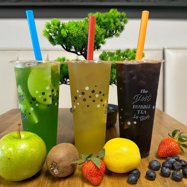 Three MISO bubble tea drinks, green, yellow, and dark, with fresh fruit on a wooden table.