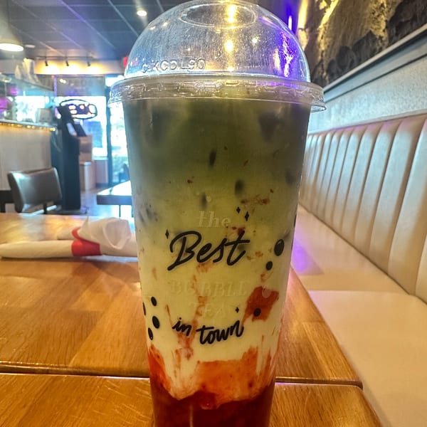 A MISO Ramen and Poke Bar bubble tea with green, white, and red layers on a wooden table.
