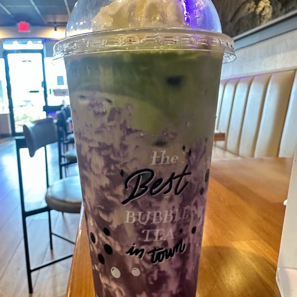 A purple and green bubble tea with whipped cream, labeled "The Best Bubble Tea in town" on a wooden table.
