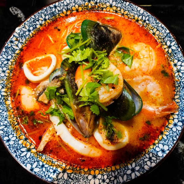 Spicy seafood ramen with shrimp, mussels, squid, and cilantro in a decorative bowl.