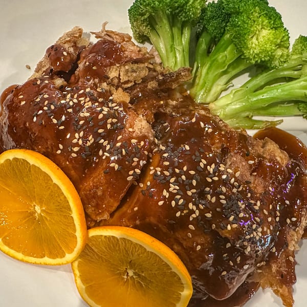 Crispy Japanese chicken with dark sauce, sesame seeds, orange slices, and broccoli.