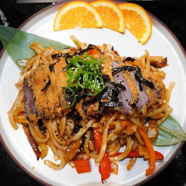 MISO Ramen and Poke Bar's Japanese udon noodles with crispy beef, garnished with scallions, seaweed, and orange slices.