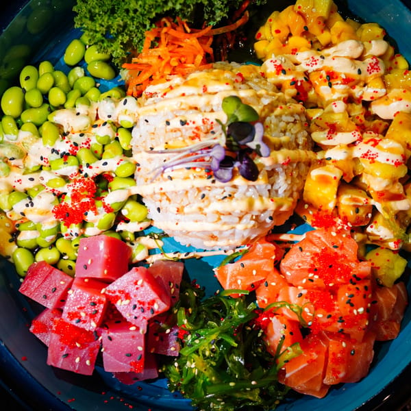 A vibrant poke bowl with tuna, salmon, edamame, mango, seaweed, and rice, drizzled with sauce.